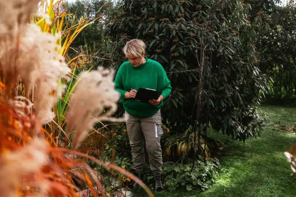 Cornelia steht bei der Bestandsaufnahme konzentriert mit ihrem Klemmbrett im Garten und fühlt sich für die Gartenplanung ein.